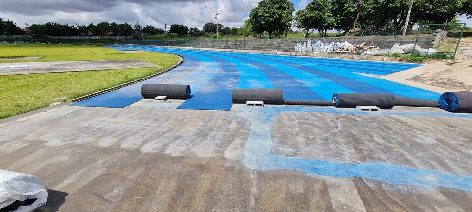 Aplicação de adesivo na pista de atletismo. A pista tem cores azul claro e azul escuro intercaladas e gramado ao centro
