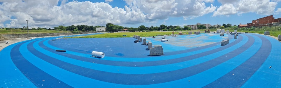 Pista de atletismo em visão panorâmica. A pista tem cores azul claro e azul escuro intercaladas e gramado ao centro